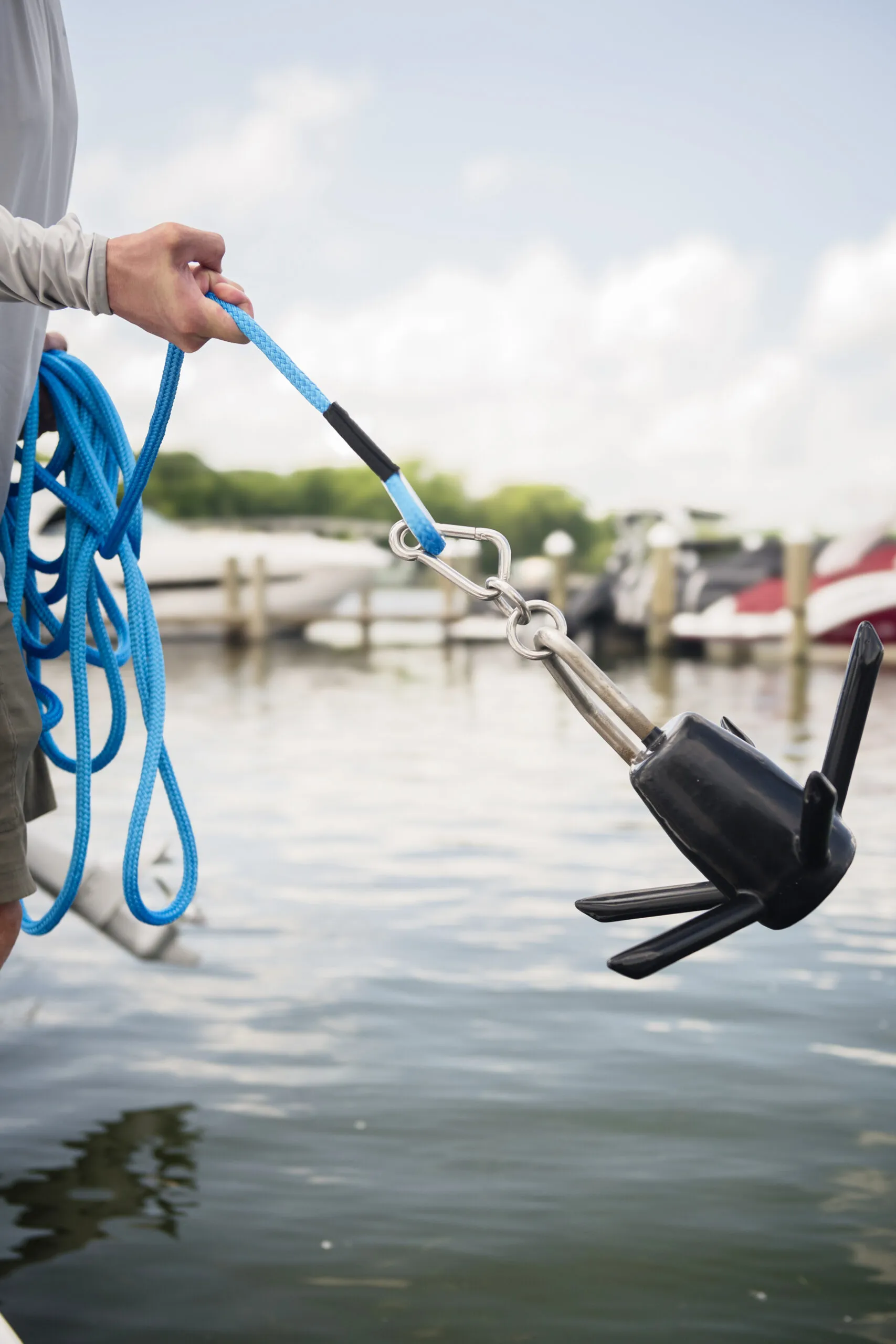 A hand holding a black boat anchor over water.